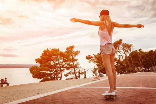 Young carefree woman riding a skateboard along the coast at sunset