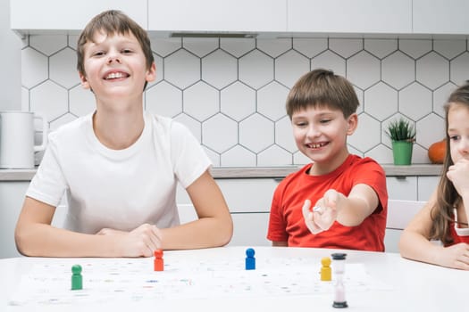 Smiling, blissful children playing board game with pieces and dice with time limit. Family fun games. Educational strategy and logic playing together. Strategic board game with dice and figures