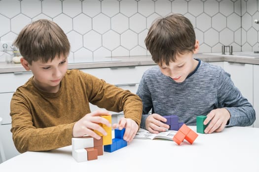 Smiling, concentrated little boys playing with colorful bricks, connect together, building figures on white table. Children reading rules and game tasks in book. Eco friendly games, plastic free