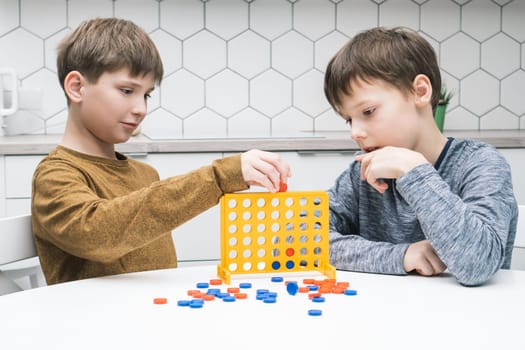 Two positive, pensive and concentrated little boys playing connect four game 3d with yellow plastic field with holes for figures on white table. Tactic and education with games. Home entertainment