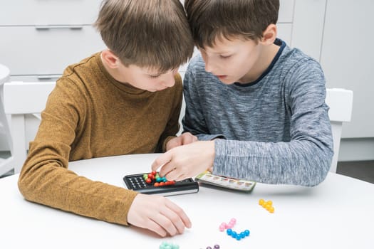 Two pensive and enthusiastic boys playing educational, strategy board game with black field and colorful balls on table. Solve riddle and find solution in puzzle games. IQ and intellectual activity