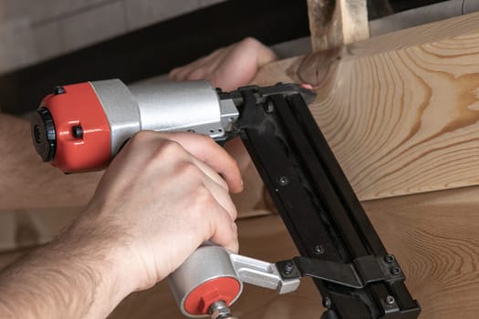 Cropped man hands using handy stapler, nail gun for wooden timber board, fastening with metal nails. Making layout on wooden plank. Woodworking and handicraft. Builder occupation, civil engineer