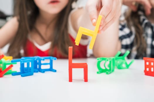 Cropped blurred little girl build pyramid tower from colorful chair toys, play chair ladder tower board game on white table. Logical and balance playing for kids with mental illness, disorder therapy