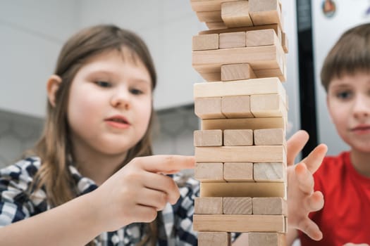 Concentrated and passionate children playing board game of balance wooden brick tower game together. Little girl slowly moving wooden block out of tower. Command battle and smart puzzle for kids.