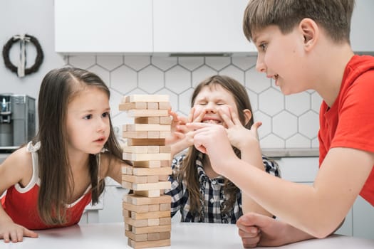Nervous and worried, passionate kids playing board balance wooden brick tower game together. Little boy trying to move wooden cube out of tower line. Children competition, training in stability puzzle
