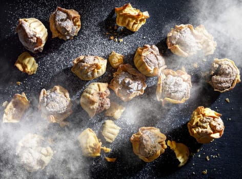 Yellow mini walnut tarts dusted with powdered sugar on a dark gray anthracite stone background