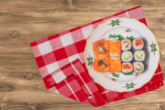 Traditional japanese sushi menu. Various kinds of sushi rolls with salmon, sashimi served on a colorful plate on red checkered napkin on rustic table. Top view. Space.