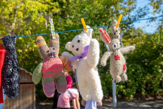 Childrens soft toys. Handmade white teddy bear and plush bunnies on clothesline over blurred natural background. Fixed with clothespins.