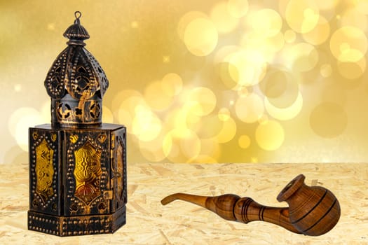 Old oriental or arabic metallic lantern and a handmade wooden tobacco pipe on table over abstract golden stars background. Ramadan Kareem template. Card design.