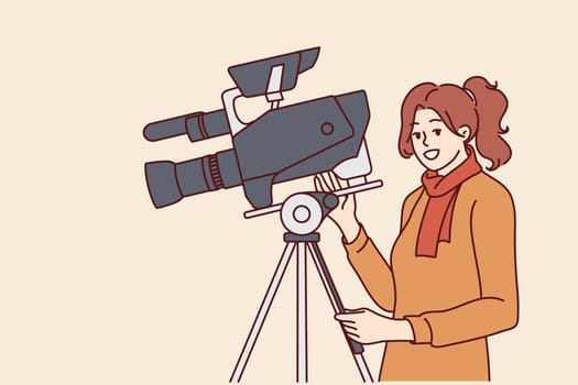 Woman videographer stands near professional video camera fixed on tripod and shoots film or news report. Girl working as producer or director in film studio uses modern filming equipment
