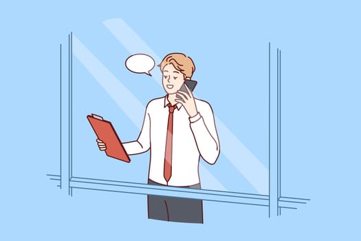 Man head of corporation is talking on phone negotiating with partners, view from behind window skyscraper. Successful guy manager or businessman holding telephone presentation to potential employees