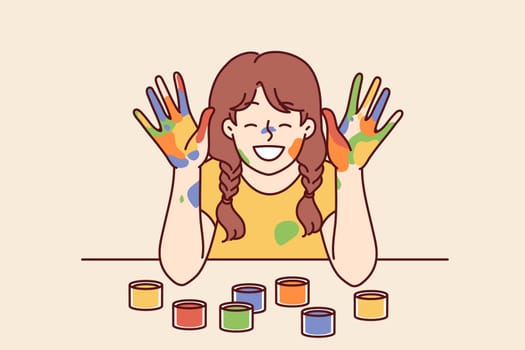 Positive girl with face and palms smeared with multi-colored paint smiles, wanting to become artist or designer. Smiling girl with gouache or watercolor on hands rejoices at school art lesson
