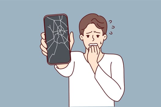 Man reacts emotionally to broken phone by bringing hand to mouth and experiencing shock due to breakdown. Guy with broken smartphone needs to replace display matrix by service center employees