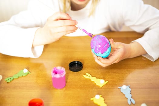 Child hands painting colored eggs for Easter on the wooden table at home. Happy Easter. Preparation for Easter celebration. High quality photo.