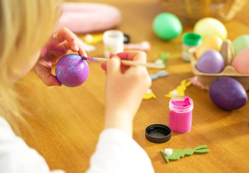 Little child hands painting colored Easter eggs on the wooden table at home. Happy Easter. Preparation for Easter celebration. High quality photo.