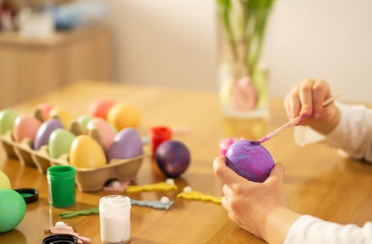 Child hands painting colored Easter eggs on the wooden table at home. Happy Easter. Preparation for Easter celebration. High quality photo.