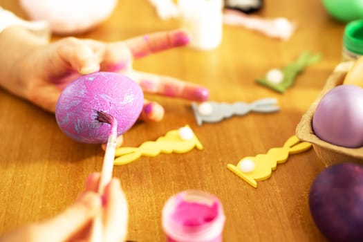 Child hands painting colored Easter eggs on the wooden table at home. Happy Easter. Preparation for Easter. High quality photo.