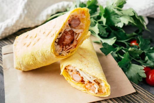 Roll with sausages and vegetables. Hot dog in pita bread on craft paper on wooden dark background with cherry tomatoes and green parsley