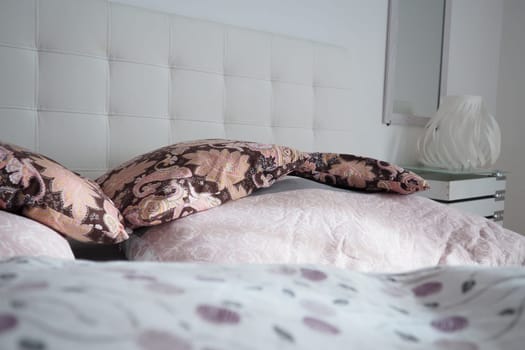 Pink decorative pillows on the bed linen. Double bridal bed with pillows and thick feather duvet. Bedroom design. Soft white headboard. Interior with furniture and bedding