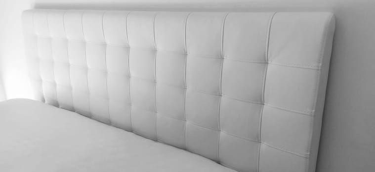 Soft headboard. Upholstery for furniture made of genuine or artificial leather and quilted fabric. Soft headboard against a light wall. Black and white monochrome photo.