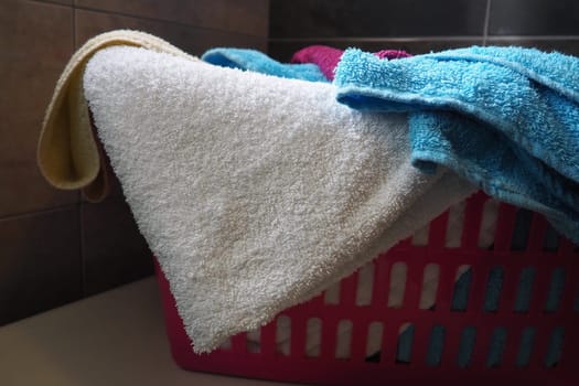 Towels in the laundry basket. Blue and pink cotton terry towels are thrown into a pink plastic basket. Housekeeping. Storing and separating laundry before washing. Light from above from an open window