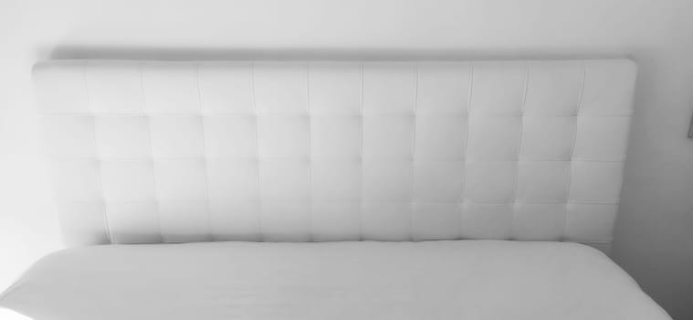 Soft headboard. Upholstery for furniture made of genuine or artificial leather and quilted fabric. Soft headboard against a light wall. Black and white monochrome photo.