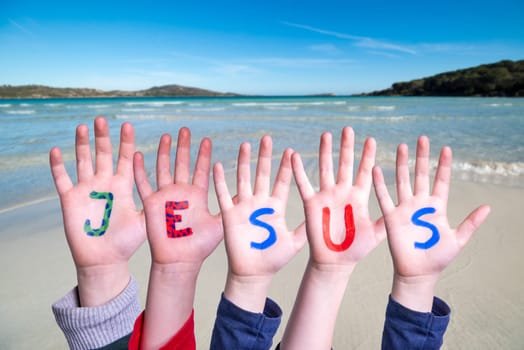 Children Hands Building Colorful English Word Jesus. Summer Ocean, Sea And Beach As Background