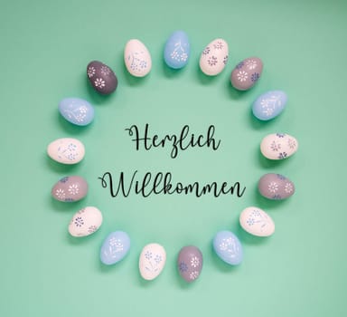 Flat Lay With German Text Herzlich Willkommen Means Welcome. Easter Egg Arrangement, Decoration And Ornament. Light Green Paper Background
