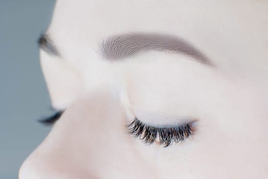 Close-up of closed eyes with long false eyelashes, perfect skin, flawless eyebrows of unrecognizable young woman. Macro shot. Eyelash extension, beauty procedures, cosmetology, visage, microblading.