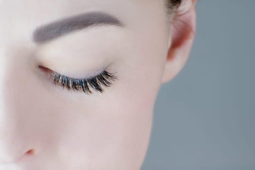 Close-up of closed eye with magnificent long eyelashes, flawless skin, ideal eyebrow of unrecognizable young woman. Macro shot. Eyelash extension, beauty procedures, cosmetics, make-up, microblading.