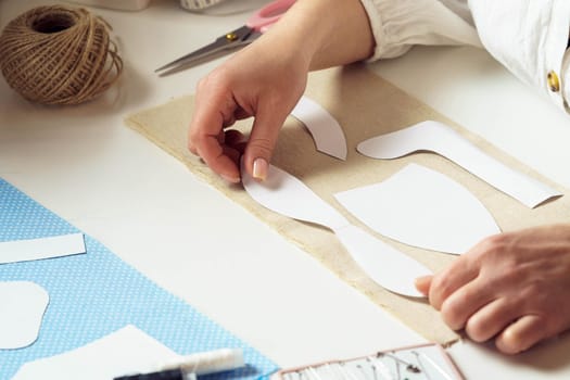 Unrecognizable close up women, seamstresses holding and placing paper sewing patterns, templates on textile sheet in workshop. Making patterns for clothing or toys. Needlework, thread sewing process