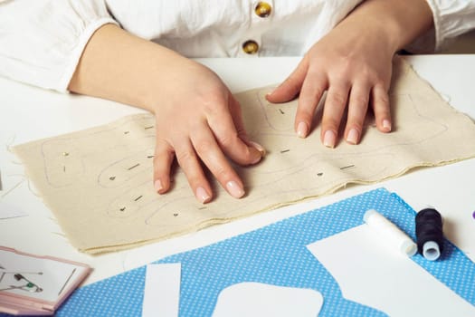 Cropped woman seamstress hands pinning and making creative sewing patterns on textile sheet on table. Needlework, thread sewing process. Sewing patterns for future toy or clothes work. Small business