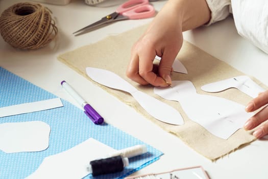 Cropped female hands taking measurements and pinning paper sewing patterns to a textile sheet on table. Embroidering thread and needlework process. Sewing patterns for future toys or clothes.
