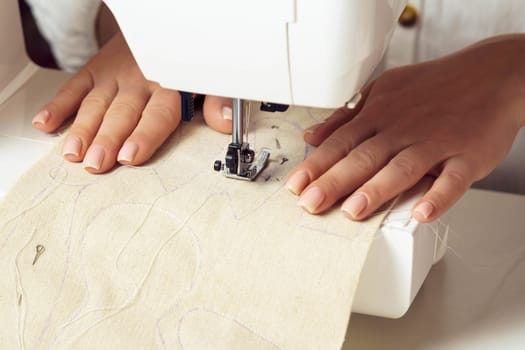 Unrecognizable female tailor hands putting white fabric textile pattern with stitch contour on sewing machine needle plate. Toys, clothes templates and production. Handicraft small business.