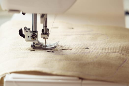 Close up beige soft fabric textile pattern with stitch contour on sewing machine needle plate under shearer fork. Hobby and DIY craft. Toys, clothes production in workshop. Handicraft small business