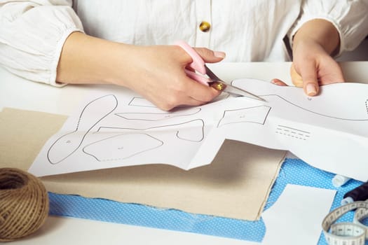 Handcrafted, do it yourself tutorial. Unrecognizable female tailor hands cutting out different shapes, patterns from paper for future clothes and toy sewing design projects. Textile production