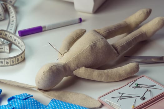 Stuffed rabbit toy with needles lying on table. Knitting hobby and business. Small hare toy next to sewing measure tape and sewing stuff. Do it yourself, children present for holidays. Creative gift