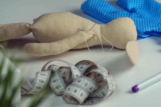 Sewing process of stuffed rabbit toy with needles in body lying on table. Knitting hobby. Hare toy near blue polka dot textile near measure tape and marker. Toys shop, store. DIY, children present