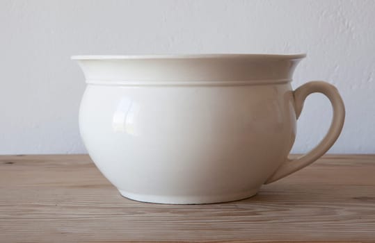 White porcelain camber pot over wooden surface. Selective focus