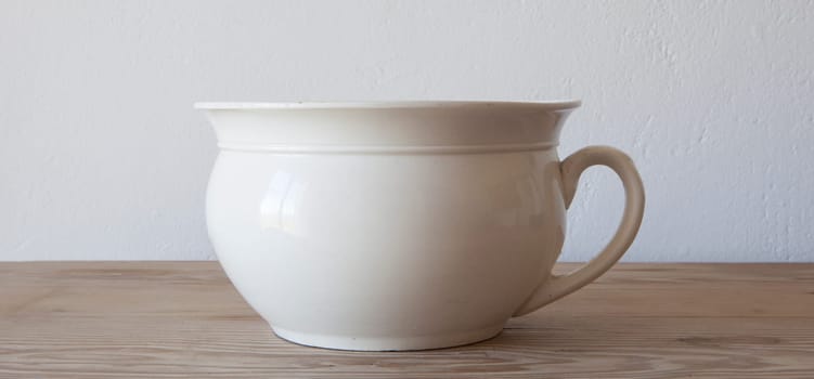 White porcelain camber pot over wooden surface. Selective focus