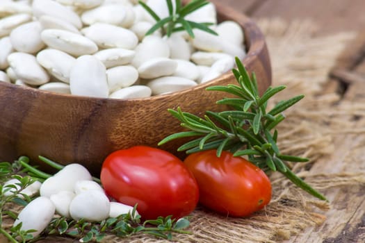 white beans, tomatoes and herbs on wooden background