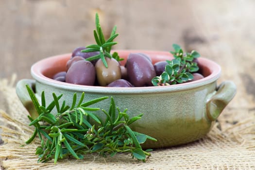 red kalamata olives and herbs in a bowl on wooden background