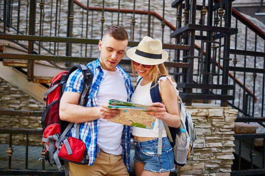 Couple with rucksacks looking at guide while traveling in foreign city