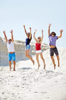 Group of ecstatic friends jumping over sandy beach