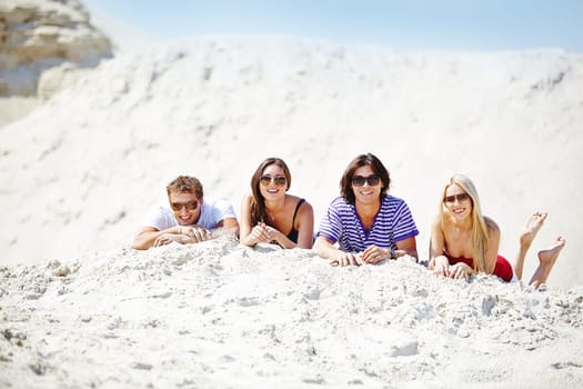 Cheerful friends in sunglasses lying on sand