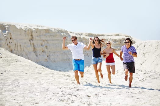 Happy friends running down sandy beach on hot day