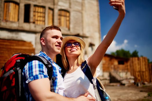 Happy young man and woman with rucksacks making selfie on background of historic building