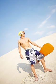 Fit young man with sandboard spending leisure on beach