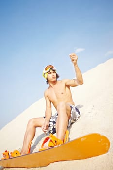 Young sportsman with sandboard sitting on beach