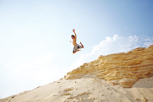 Handsome guy in jump over sandy beach against sky
